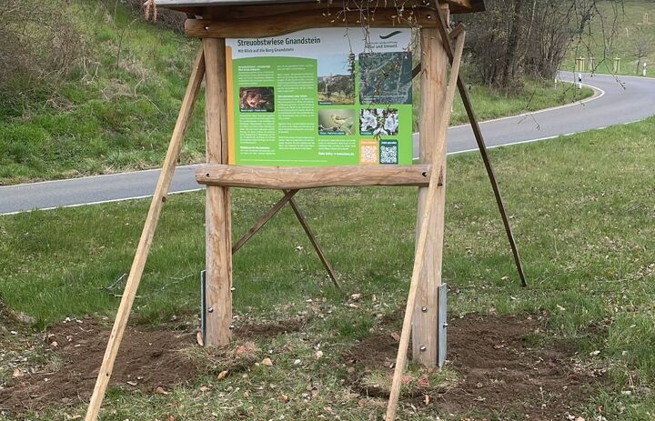 Blick auf die im Jahr 2025 errichtete Gebietstafel mit der Streuobstwiese im Hintergrund.