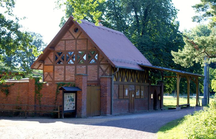 Das Bild zeigt ein Gebäude, eine Schautafel und das Eingangstor der Auwaldstation Leipzig.