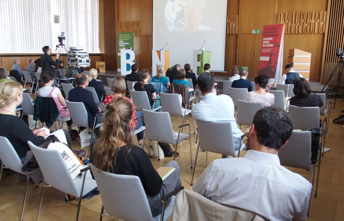 Eindrücke vom Fachtag BNE am 21. Juni 2022. Teilnehmende sitzen im Saal auf Stühlen und verfolgen Präsentation auf einer Leinwand.