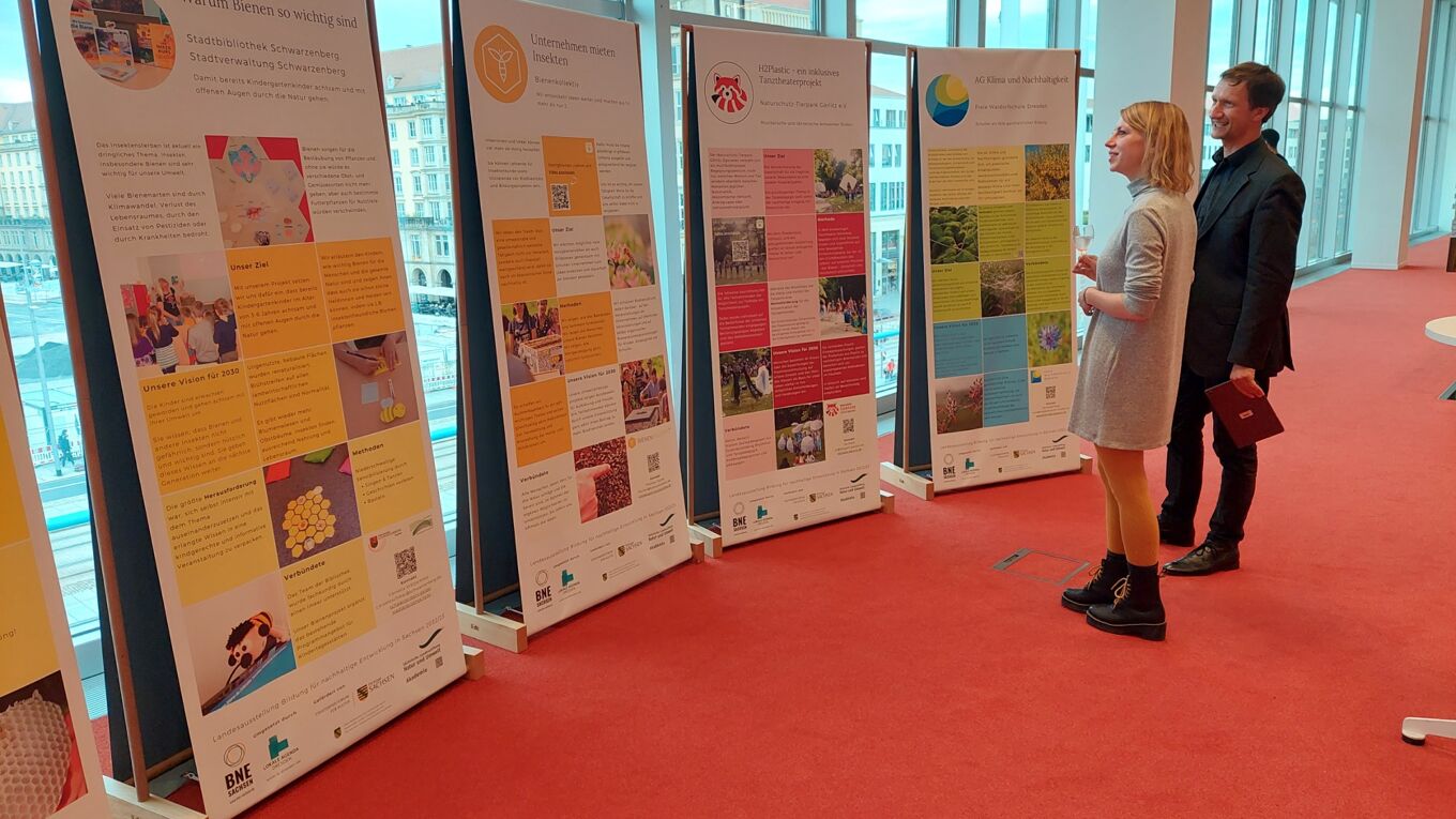 Zwei Personen schauen sich 4 Banner der sächsischen Landesausstellung Bildung für nachhaltige Entwicklung 2022/2023 an, welche im Foyer der Zentralbibliothek des Kulturpalastes Dresden aufgebaut ist.