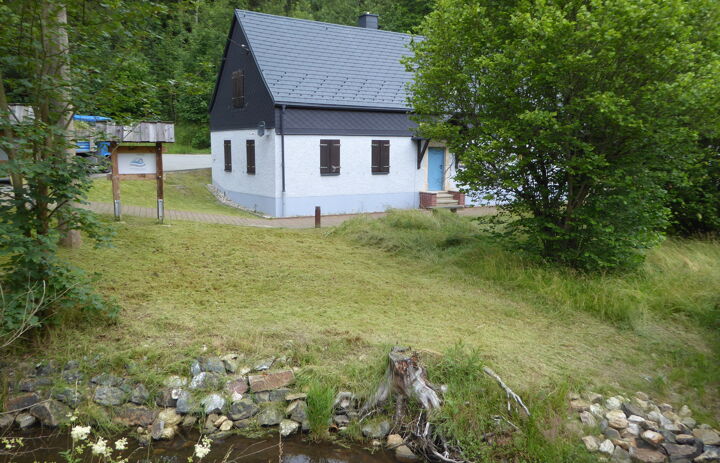 Foto der Flussperlmuschelzuchtstation. Ein weißes Gebäude mit schwarzem Dach in der Größe eines Einfamilienhauses. Im Vordergrund ein Bach.