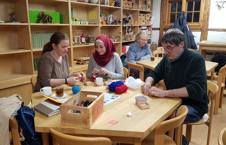 Teilnehmende eines Seminars basteln an Holztischen.