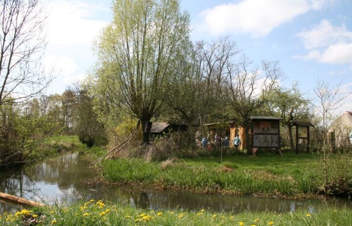 Zu sehen sind die Hütten und Infotafeln des Biberhofs Torgau unmittelbar an einem Teich gelegen. - Link: NABU-Naturschutzstation Biberhof Torgau