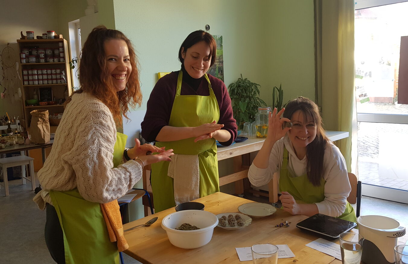 BFD-Seminar Gesunde Ernährung Drei Seminarteilnehmerinnen arbeiten an einem Tisch und bereiten eine Speise aus Saaten und Kräutern zu, eine hält lächelnd ein neu geformtes Bällchen in die Kamera