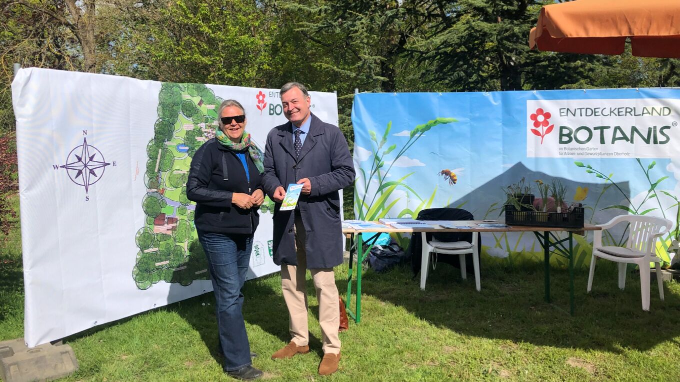 Frau Dr. Junhold und Herr Robert Clemen, Stiftungsdirektor, stehen vor Bannern mit der Karte des Botanischen Gartens und dem Logo des Entdeckerland Botanis
