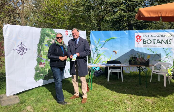 Frau Dr. Junhold und Herr Robert Clemen, Stiftungsdirektor, stehen vor Bannern mit der Karte des Botanischen Gartens und dem Logo des Entdeckerland Botanis