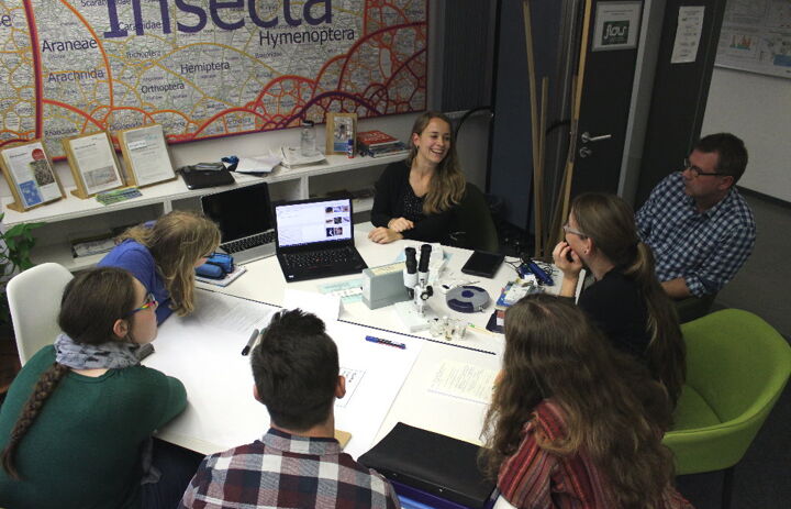 Menschen sitzen an einem Tisch und sehen auf einen Laptopbildschirm. - Link: Citizen Science-Projekt FLOW