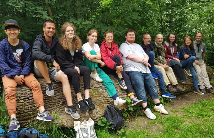 Gruppenfoto der Seminarteilnehmenden nach einer Geocaching-Tour, die lächelnd auf einem großen Baumstamm im Leipziger Auenwald posieren