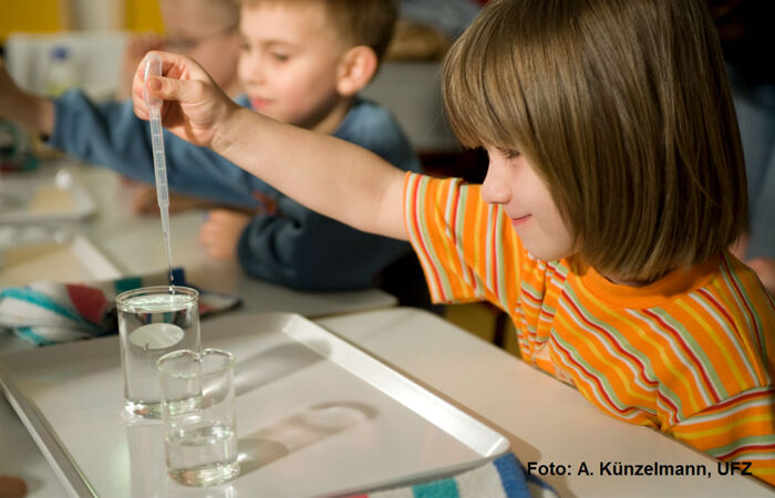 Kinder ziehen mit einer Pipette Wasser aus einem Reagenzglas.